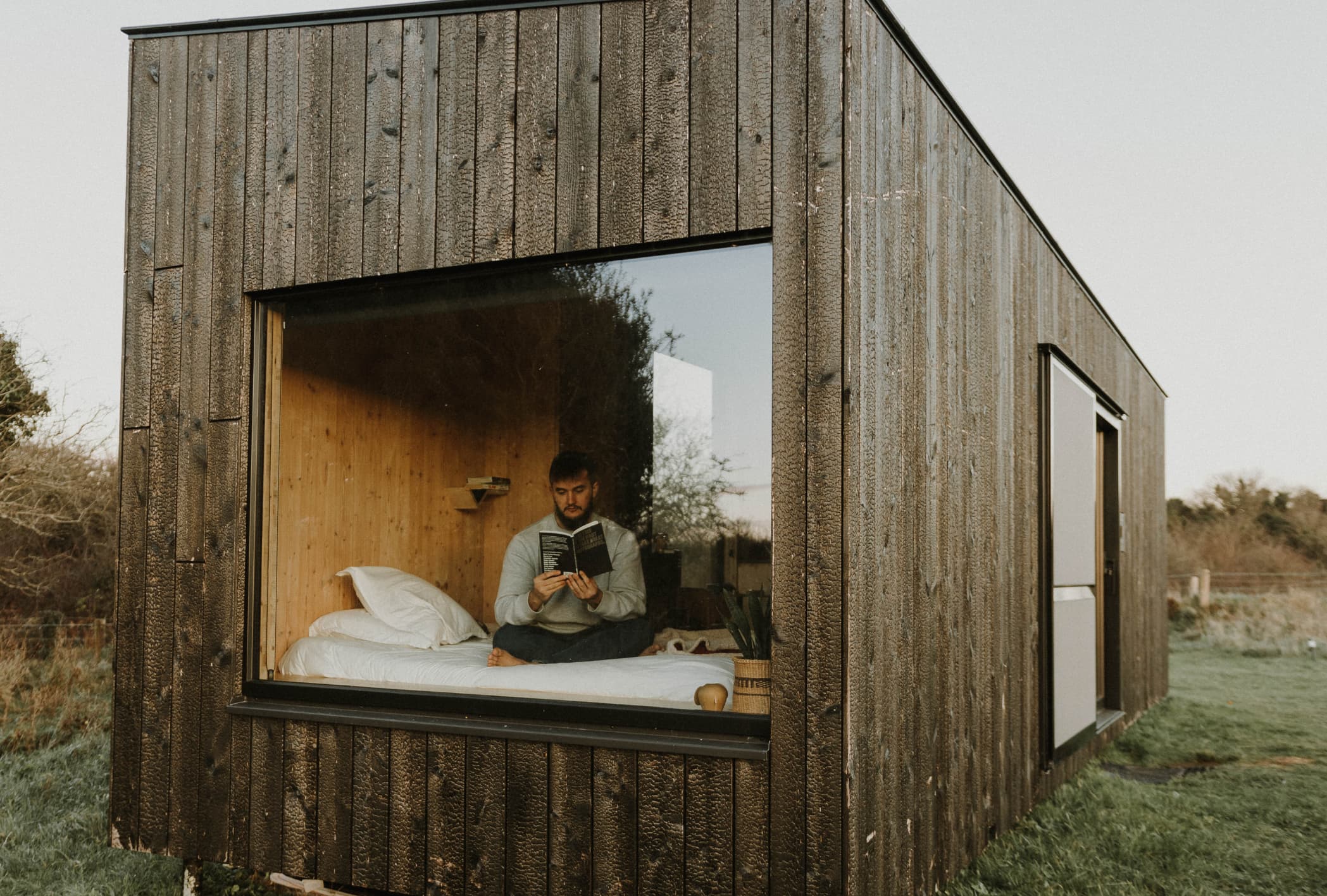 man reading a book in the window of a cabin